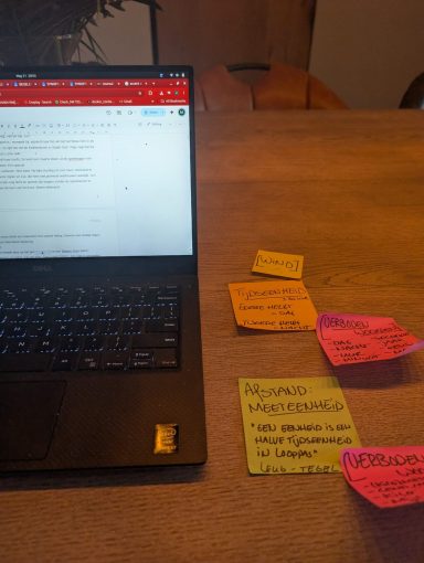 Een laptop met notitieblokjes in verschillende kleuren ernaast op een tafel.