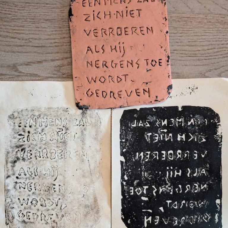 Twee platen met tekst in reliëf en contrasterende kleuren op een houten ondergrond.