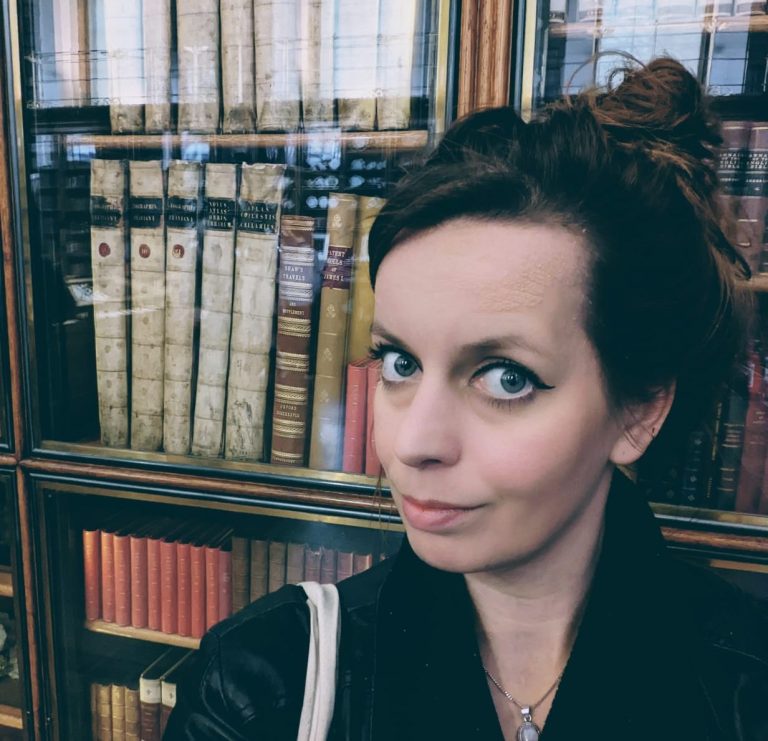 Jonge vrouw met een lichte huid en donkere haren, voor een boekenkast met oude boeken.