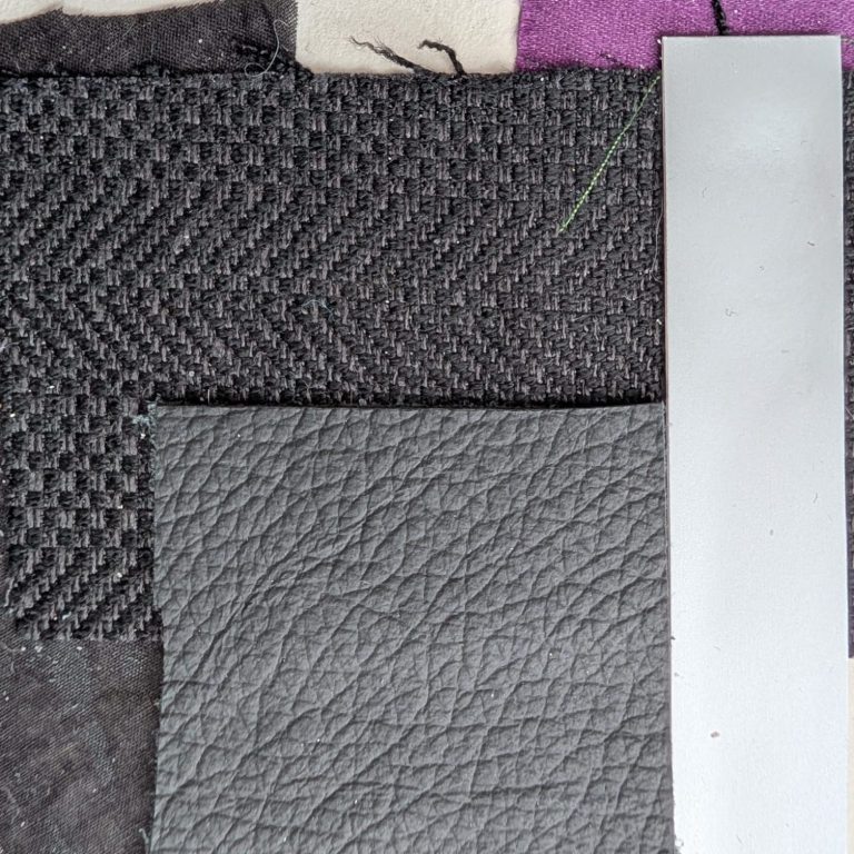 Een verzameling textiel en leer in verschillende grijstinten, met een metalen strip.